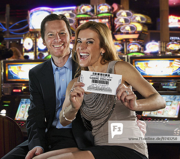 Excited Caucasian couple holding gaming voucher in casino