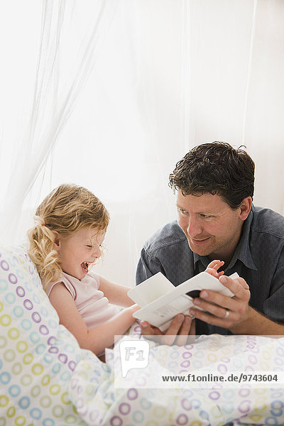 Caucasian father reading book to daughter in bed