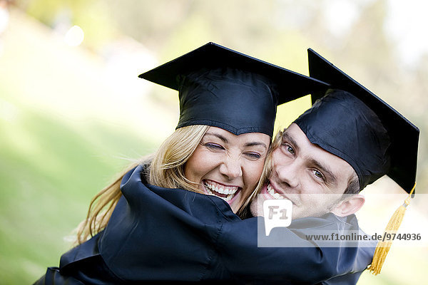 Graduating Hispanic couple in cap and gown hugging
