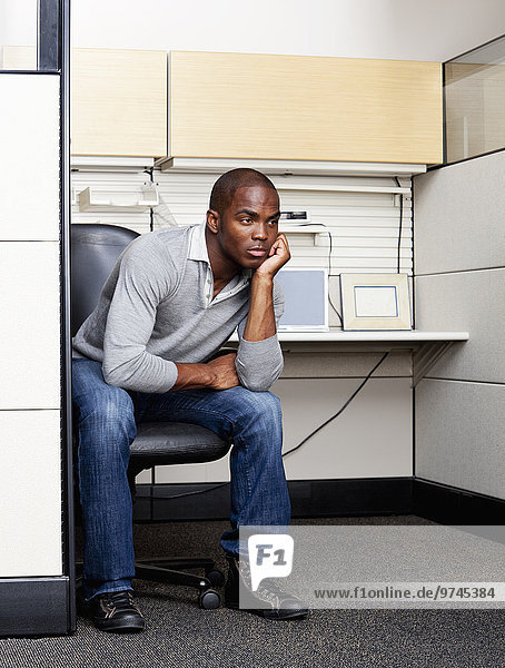 Serious mixed race man sitting in office cubicle
