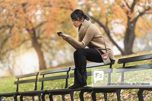 Asian woman using cell phone on park bench