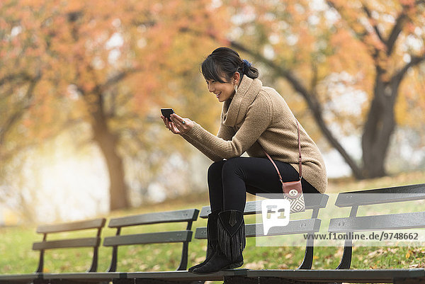 Asian woman using cell phone on park bench