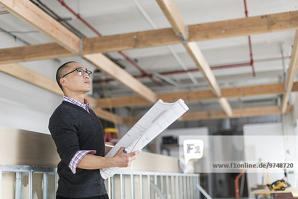 Korean architect holding blueprints and examining ceiling
