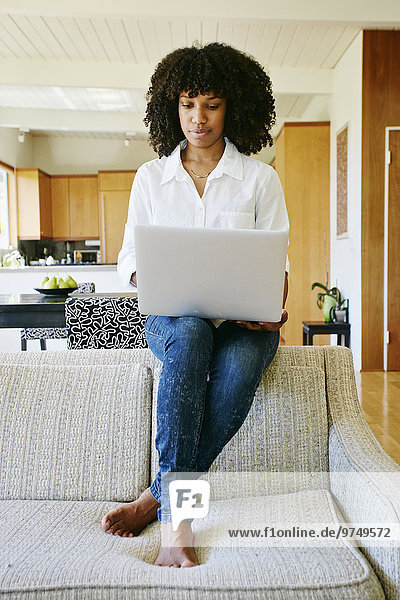 Mixed race woman using laptop on sofa