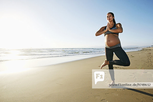 Pregnant Hispanic woman practicing yoga on beach