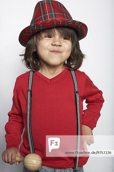 Porträt eines lächelnden kleinen Jungen mit hölzerner Rassel mit Hut und Hosenträgern