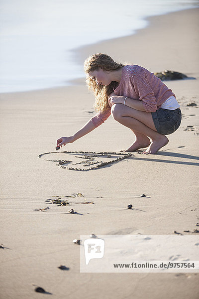 Junge Frau zeichnet Herz im Sand am Strand
