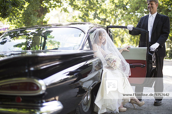 Braut steigt vor ihrer Hochzeit mit Fahrer aus dem Auto aus.