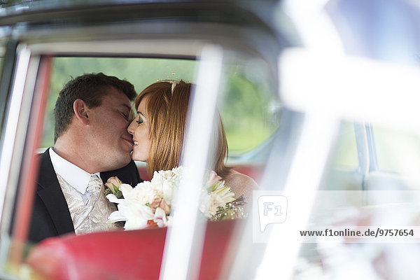 Fröhliches Brautpaar beim Küssen im Auto