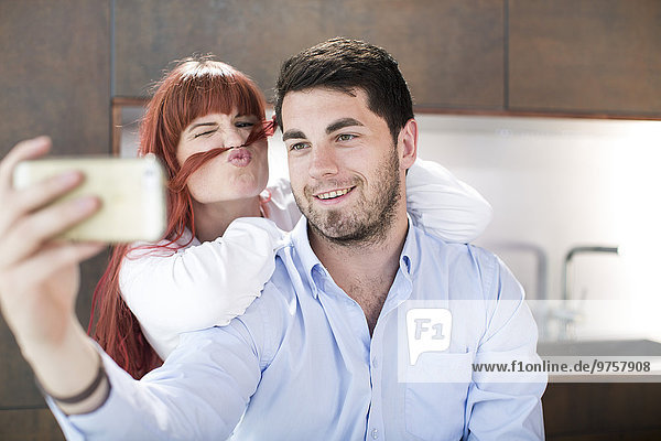 Playful couple in kitchen taking a selfie