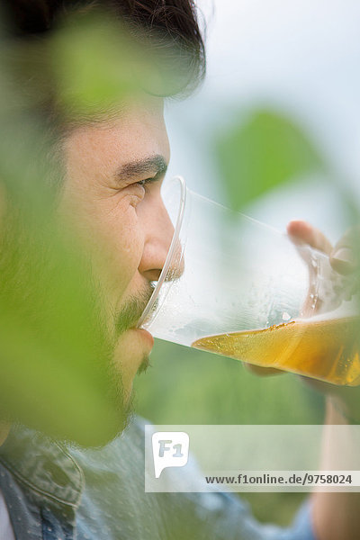 Junger Mann trinkt Bier aus Plastikbecher im Freien