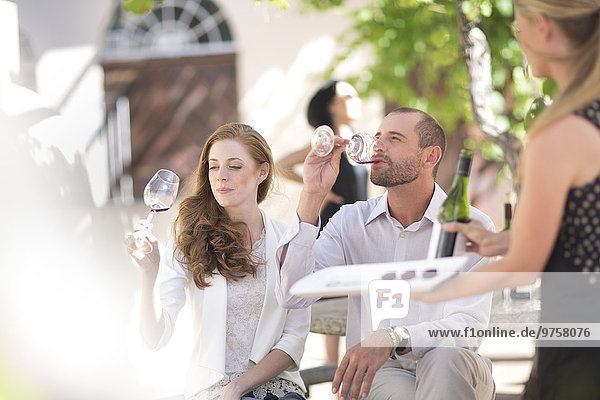 Kellnerin mit Tablett und Paar im Freien sitzend  Rotweinverkostung