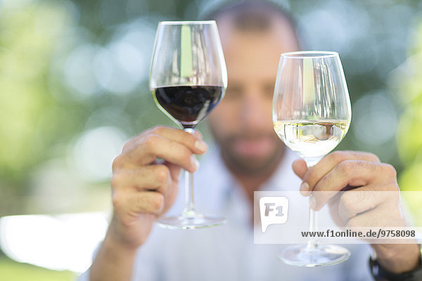 Mann vergleicht Weißwein und Rotwein bei einer Weinprobe