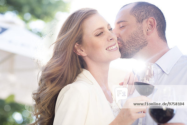 Happy couple holding wine glasses and kissing outdoors