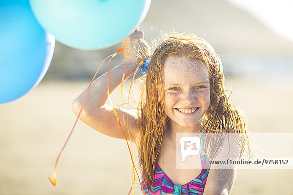 Mädchen am Strand lächelt und hält Luftballons