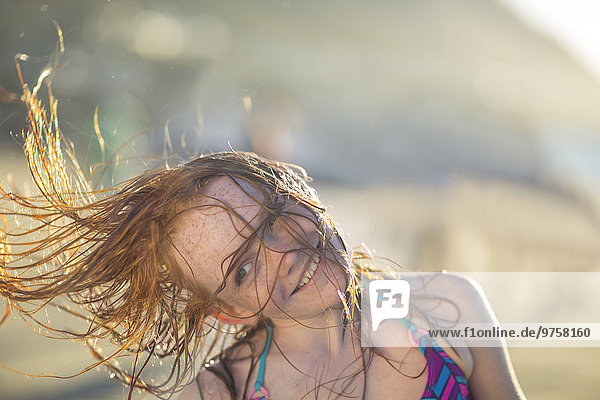 Mädchen am Strand lächelt und schwingt ihre Haare in den Wind.