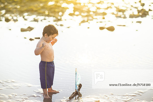 Junge spielt mit einem Spielzeug-Holzboot im Wasser