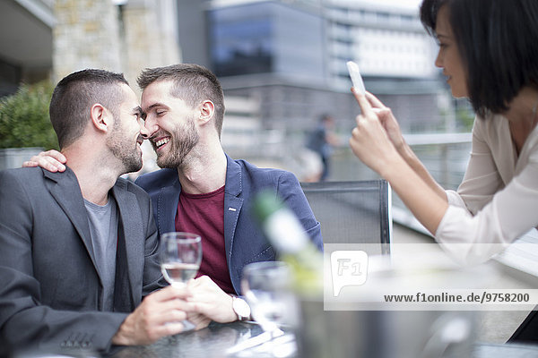 Schwules Paar beim Essen und Freund beim Fotografieren mit dem Handy