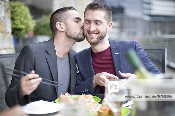 Schwules Paar küsst und isst Sushi im Außenrestaurant