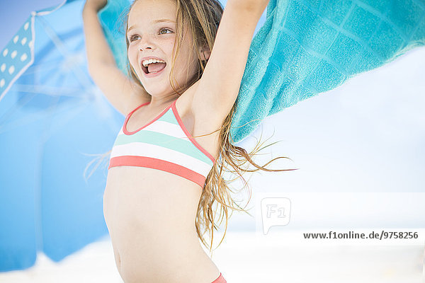 Lächelndes Mädchen am Strand trocknet mit einem Strandtuch ab