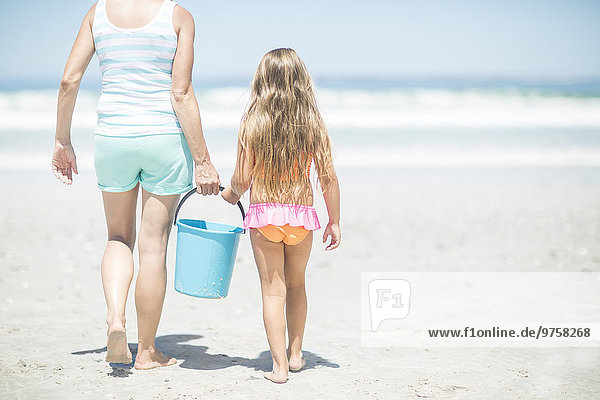 Mutter und Tochter am Strand spazieren gehen mit einem Eimer