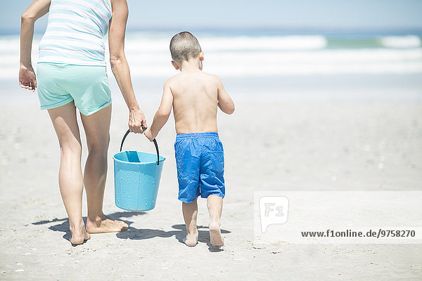Mutter und Sohn am Strand wandern mit einem Eimer