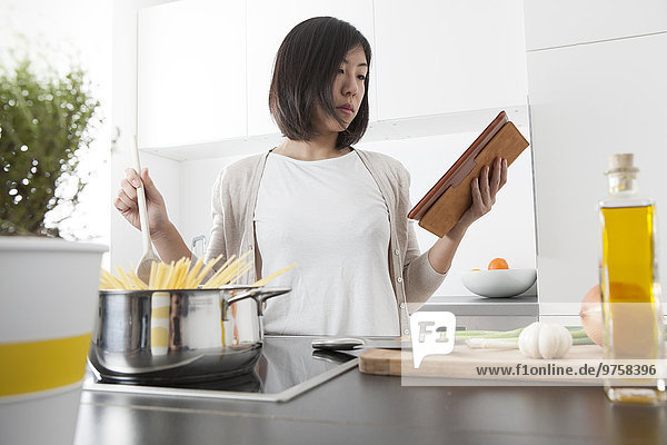 Junge Frau beim Kochen von Spaghetti mit digitalen Tabletten