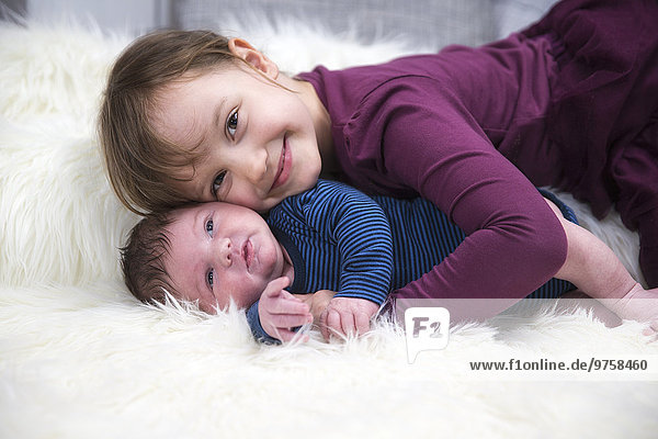 Lächelndes kleines Mädchen mit neugeborenem Bruder auf Schaffell