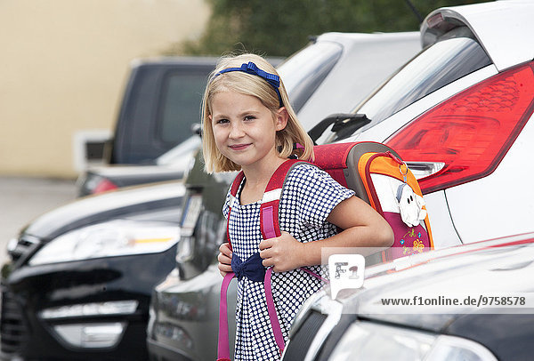 Portrait of little girl with school bag between parking cars