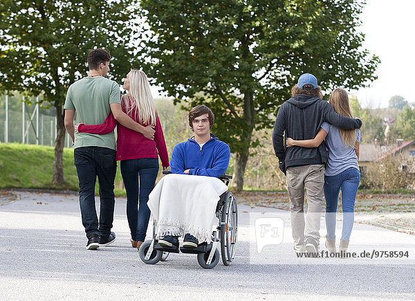 Zwei junge Paare Arm in Arm und junger Rollstuhlfahrer allein