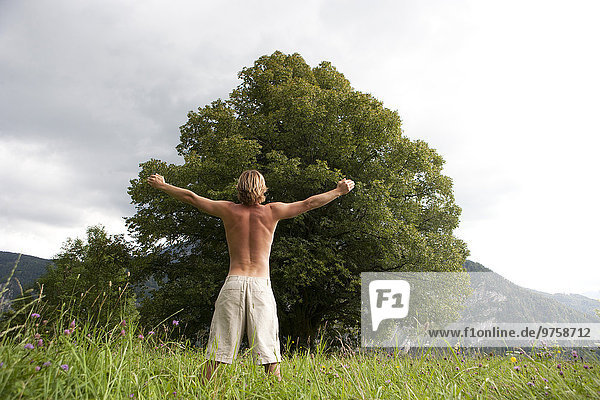 Österreich  Salzkammergut  Mondsee  Mann mit ausgestrecktem Arm vor einem alten Baum stehend