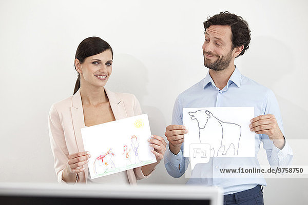 Businesswoman holding child's drawing and businessman holding paper with bull figure