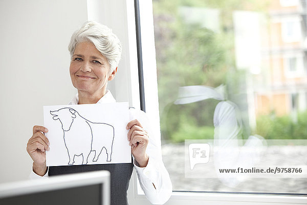 Smiling mature businesswoman holding paper with bull figure