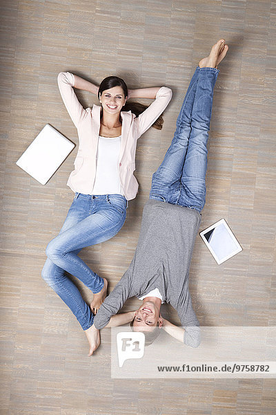 Lächelnder Mann und Frau auf dem Boden liegend mit Laptop und digitalem Tablett