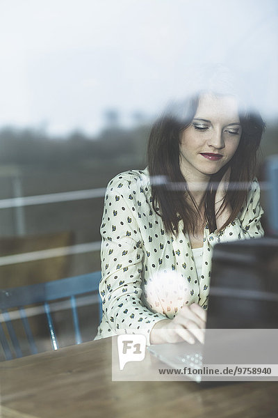Junge Frau hinter der Fensterscheibe mit Laptop