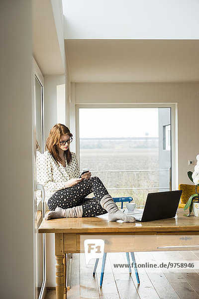 Junge Frau mit Handy auf Holztisch sitzend
