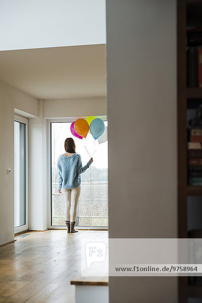 Junge Frau hält einen Haufen Luftballons  die aus dem Fenster schauen.
