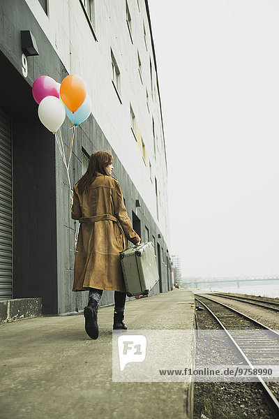 Junge Frau mit Koffer mit Ballonbund auf Plattform