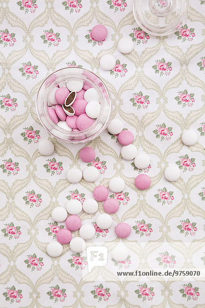 Glas mit rosa und weißen Schokoladenknöpfen auf floral gemustertem Stoff