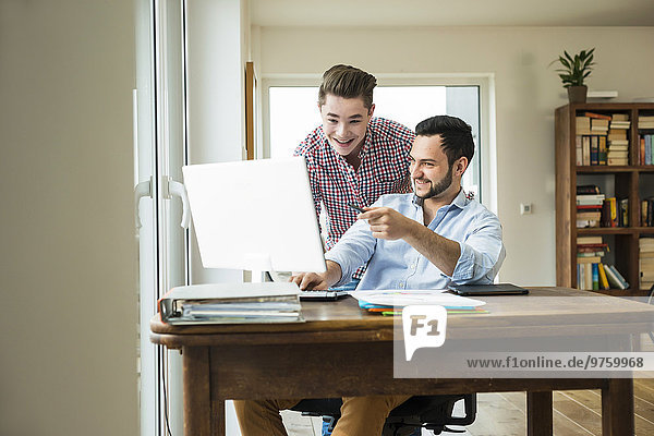 Two smiling young men looking at computer monitor