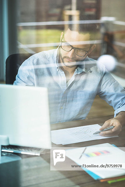 Junger Mann hinter der Fensterscheibe bei der Arbeit am Computer