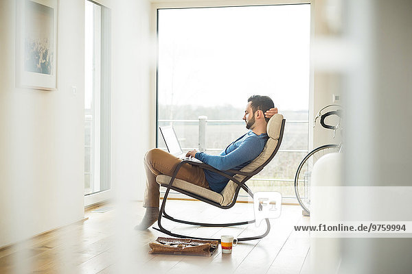 Young man sitting on rocking chair using laptop