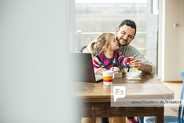 Vater und Tochter mit Laptop und Spiel am Holztisch
