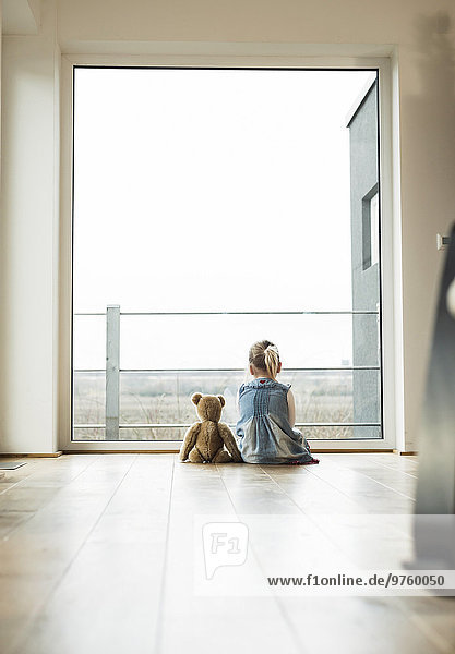 Girl sitting next to teddy looking out of window