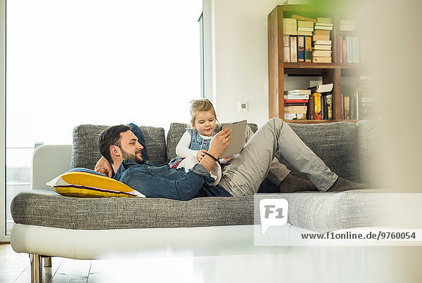 Father and daughter with digital tablet on sofa