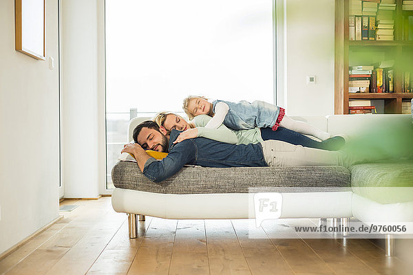 Family lying on couch on top of each other with closed eyes