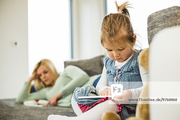 Girl using digital tablet on couch with mother in background