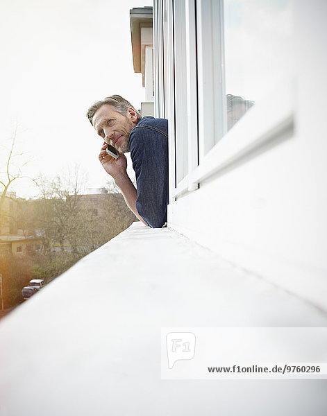 Deutschland  Köln  Mann aus dem Fenster gelehnt mit dem Handy
