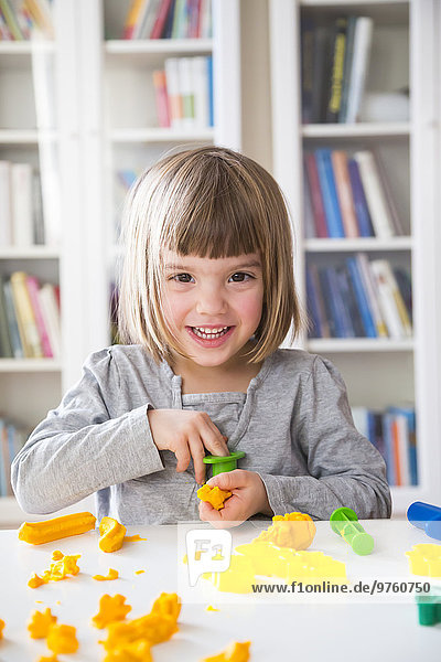 Portrait of smiling little girl playing with yellow modeling clay