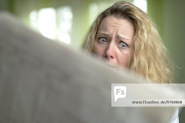 Horrified woman reading newspaper